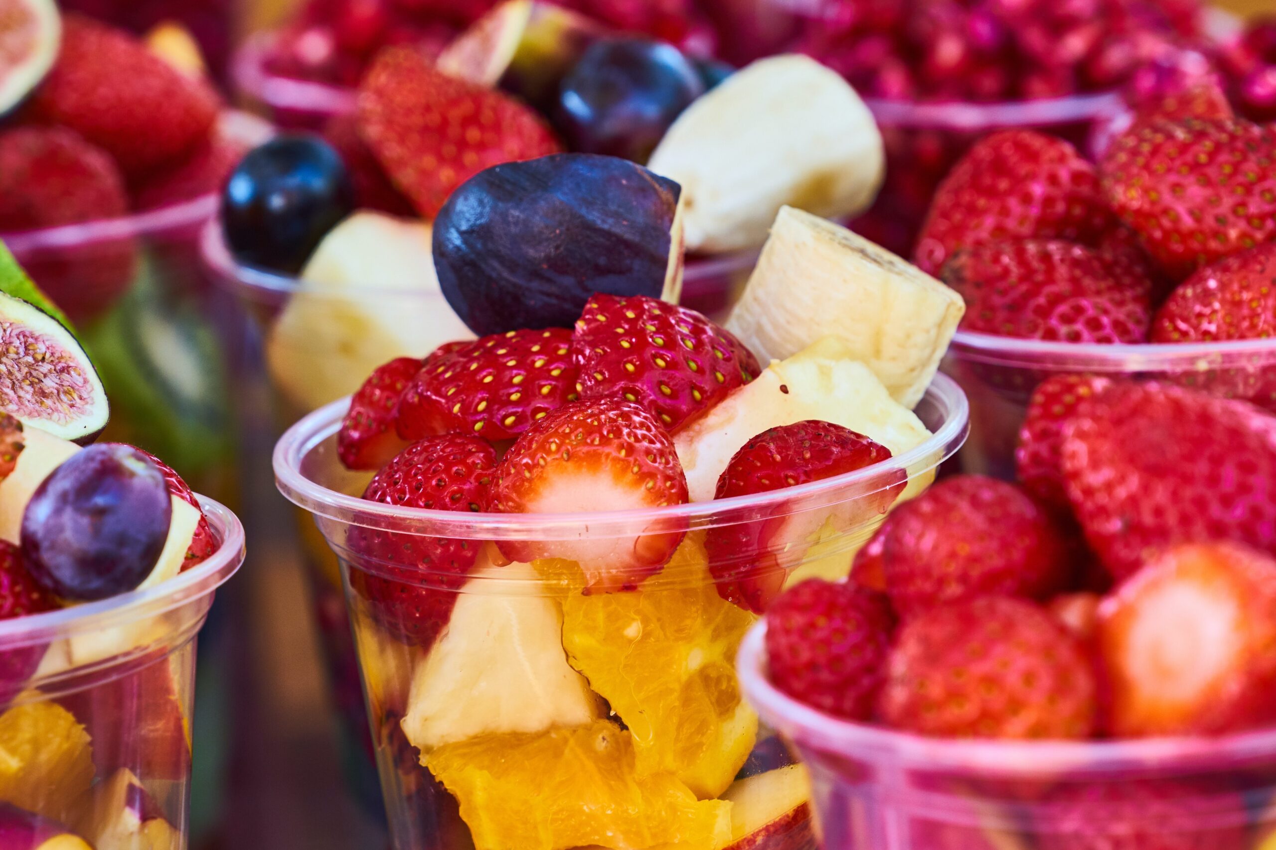Nine clear plastic cups filled with bight summer fruit pieces with strawberries and blueberries on top